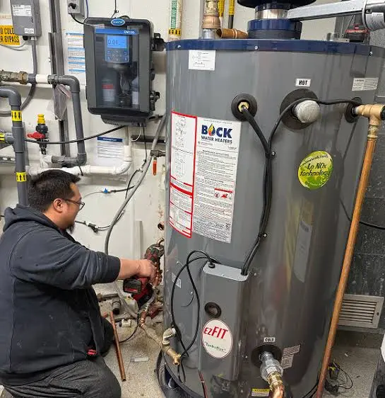 Technician servicing the gas and water connections on a commercial water heater
